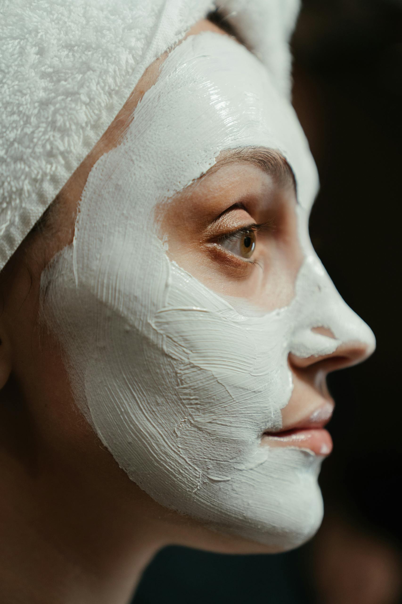Close-up portrait of a woman with a facial mask and towel, emphasizing self-care and skincare.