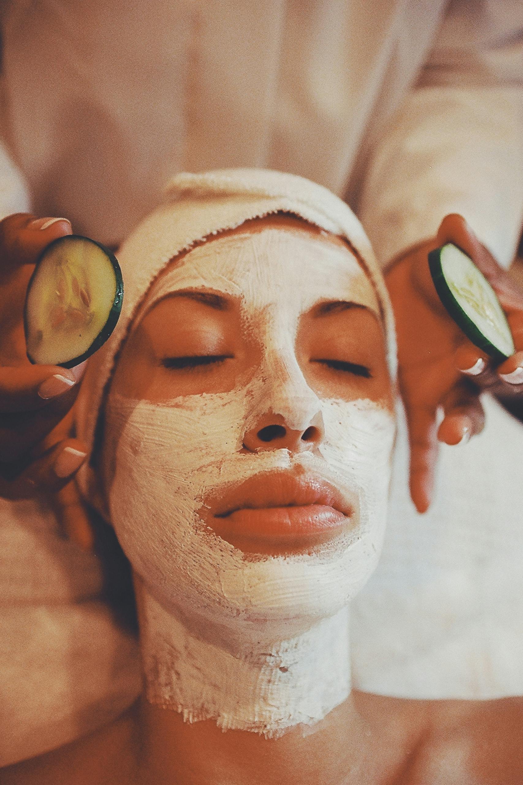 Woman receiving spa facial with face mask and cucumber slices, promoting relaxation and skincare.